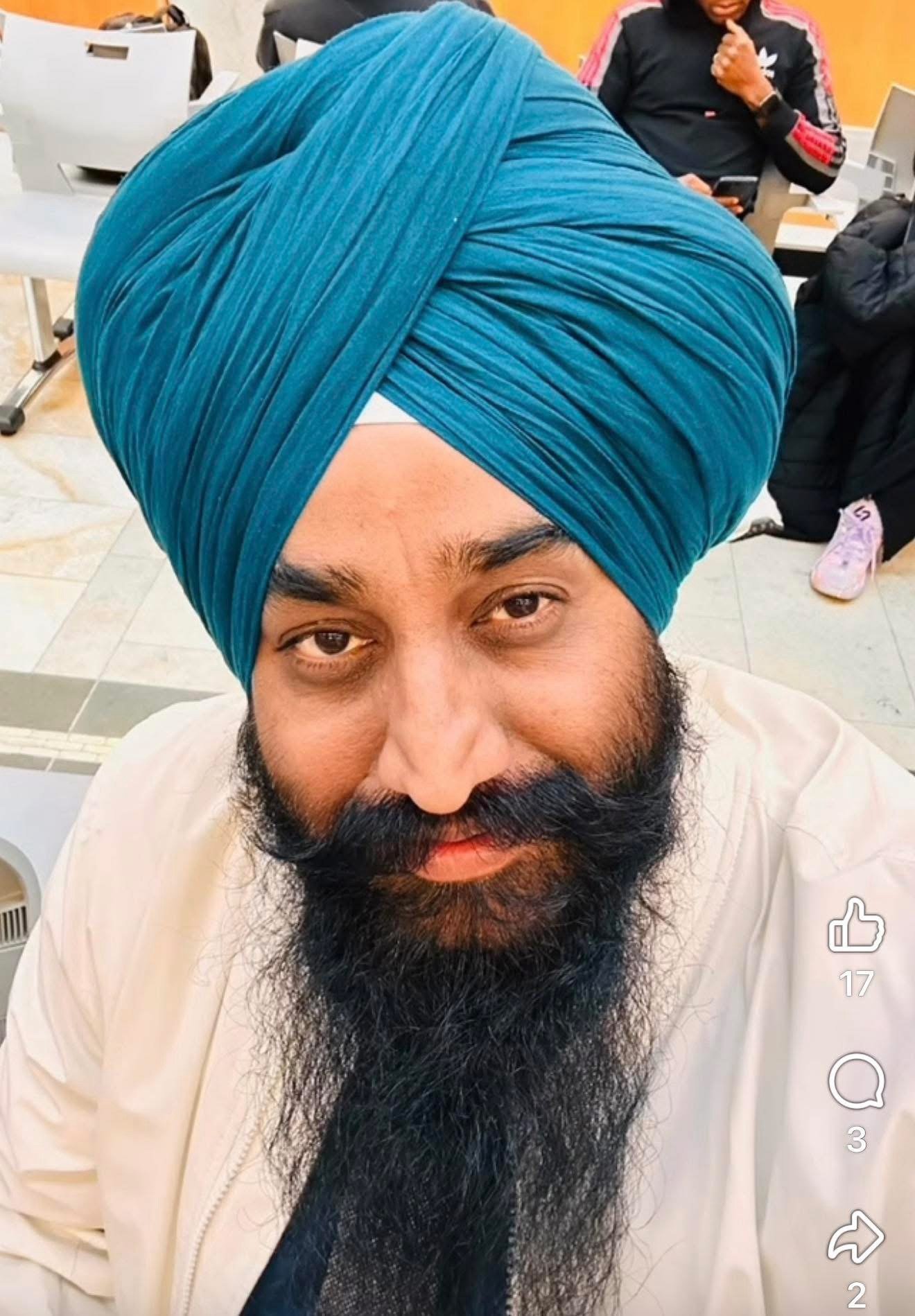 A man wearing a blue turban and white shirt takes a selfie indoors.