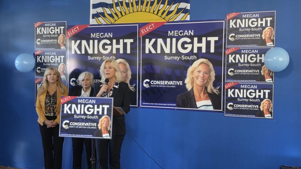 Megan Knight Campaign Launch Draws Strong Local Support in Surrey 2 A woman speaks at a lectern in front of Megan Knight campaign signs.